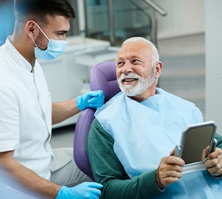 Senior patient looking at dentist while holding small mirror