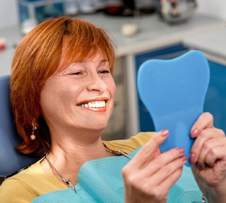 Woman at the dentist’s smiling in small mirror