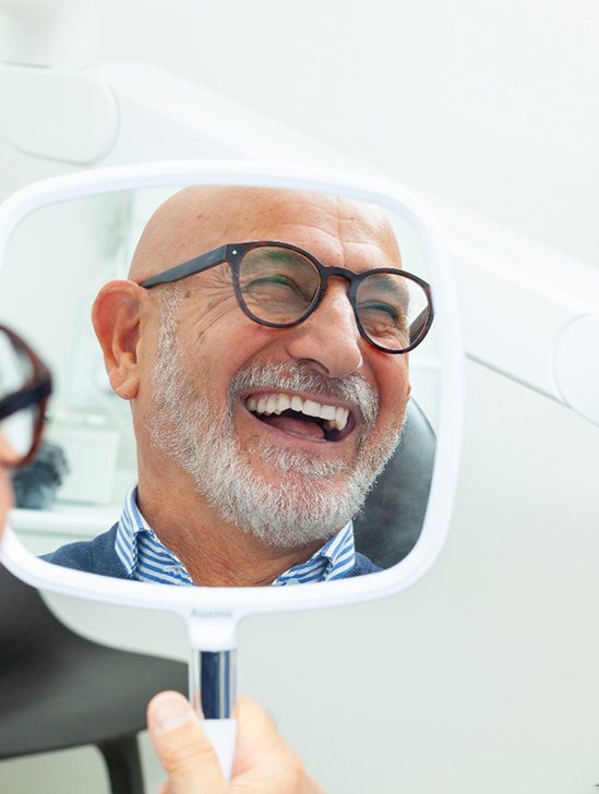 Man with glasses smiling at reflection in handheld mirror