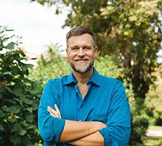 Man in blue shirt smiling outside with arms crossed