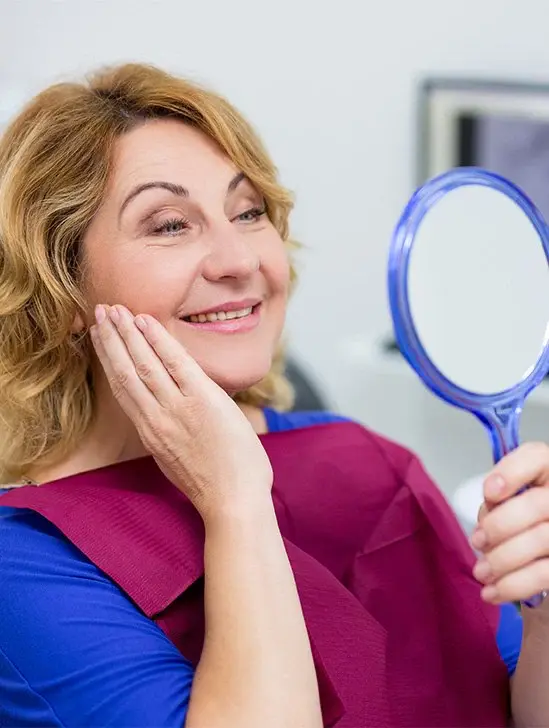 Woman checking smile in mirror after receiving dental implants in State College, PA