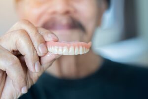 Man holding a full upper denture in his hand